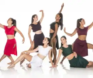 Six dancers pose in colorful costumes against white background.