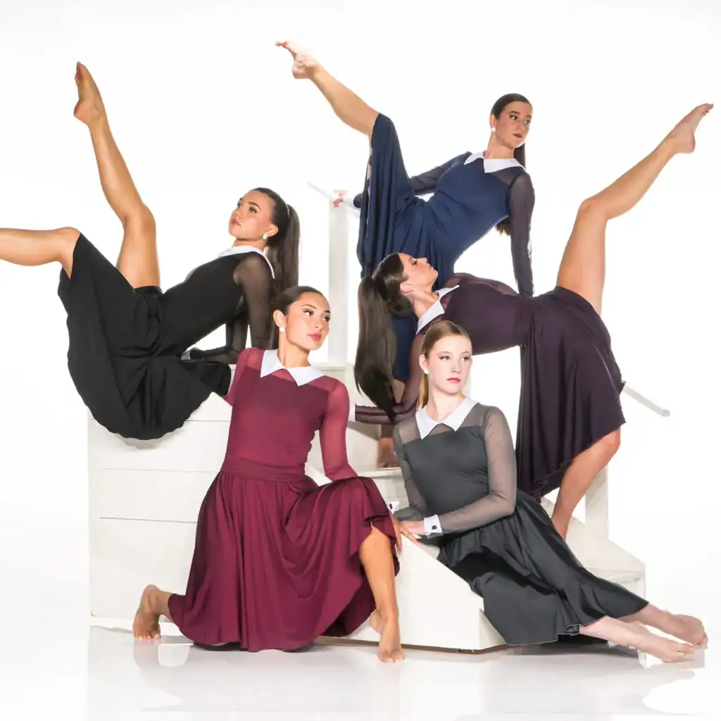 Five dancers pose on white stairs in flowing dresses
