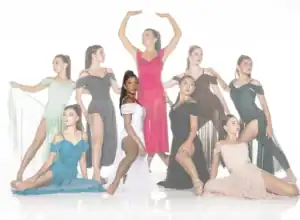 Nine dancers pose in colorful flowing dresses against white backdrop.