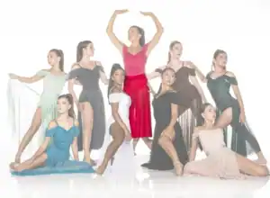 Nine dancers pose in colorful flowing costumes against white backdrop.