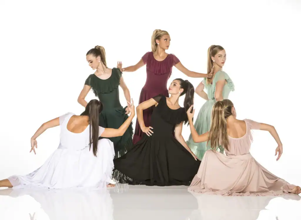 Six women pose in flowing ruffled dresses.