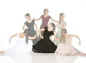 Six women pose in flowing dresses against white background.