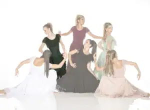 Six women pose in flowing dresses against a white background.