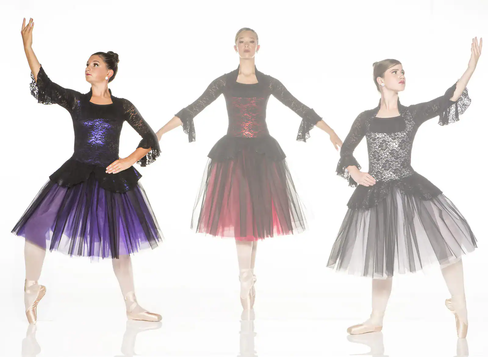 Three ballerinas pose in black lace dresses with colorful skirts.