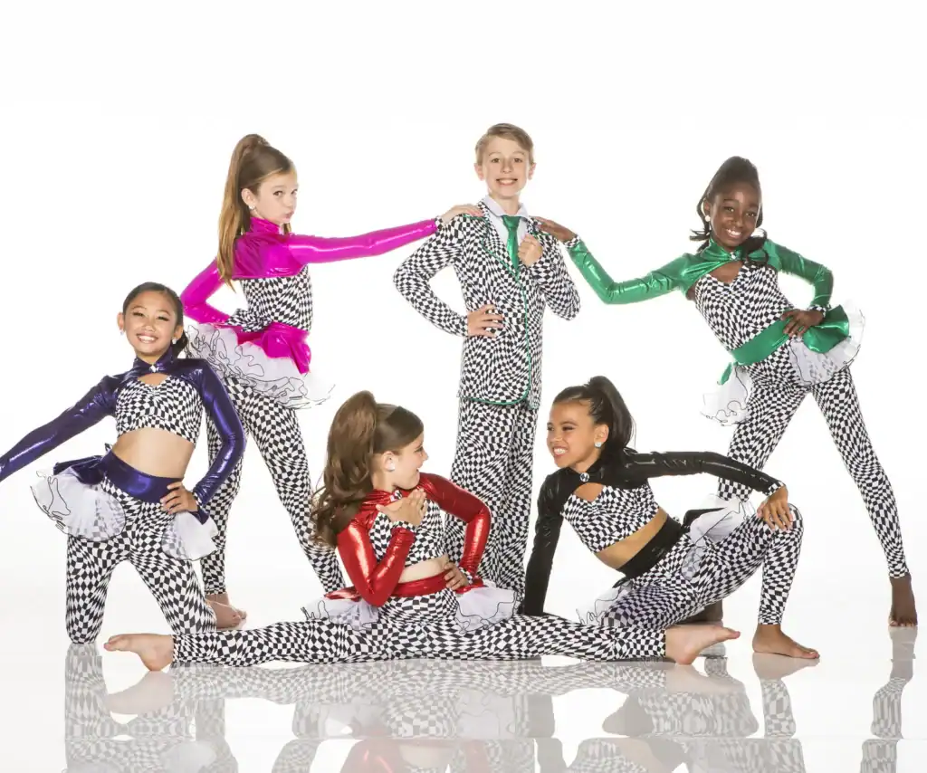 Six young dancers pose in colorful checkerboard costumes.