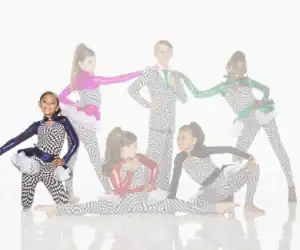 Six young dancers in checkerboard costumes pose together.