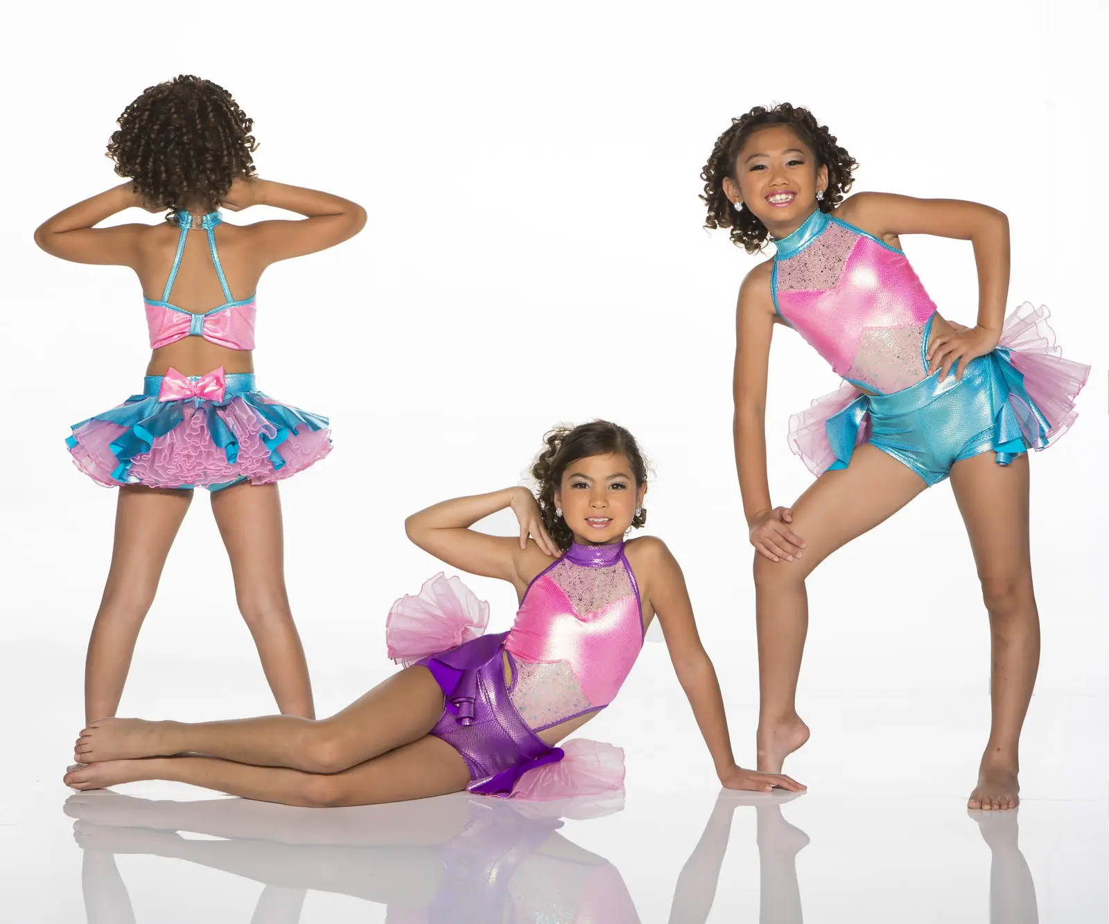 Three girls modeling colorful dance costumes against white background