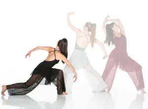 Three contemporary dancers posing in flowing dresses on white background.