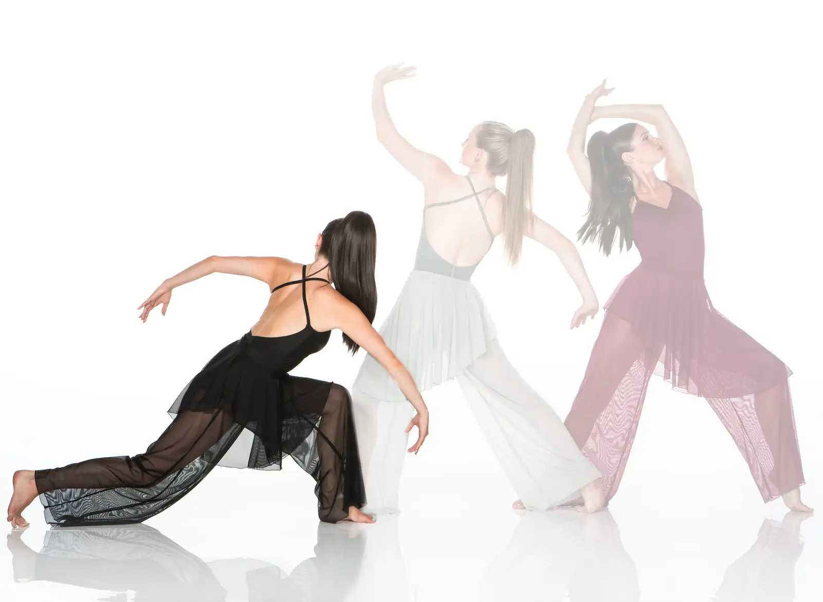 Three contemporary dancers posing in flowing dresses on white background.