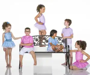 Six children in colorful gingham outfits pose around a bench.