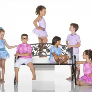 Six children in colorful gingham outfits pose around a bench.