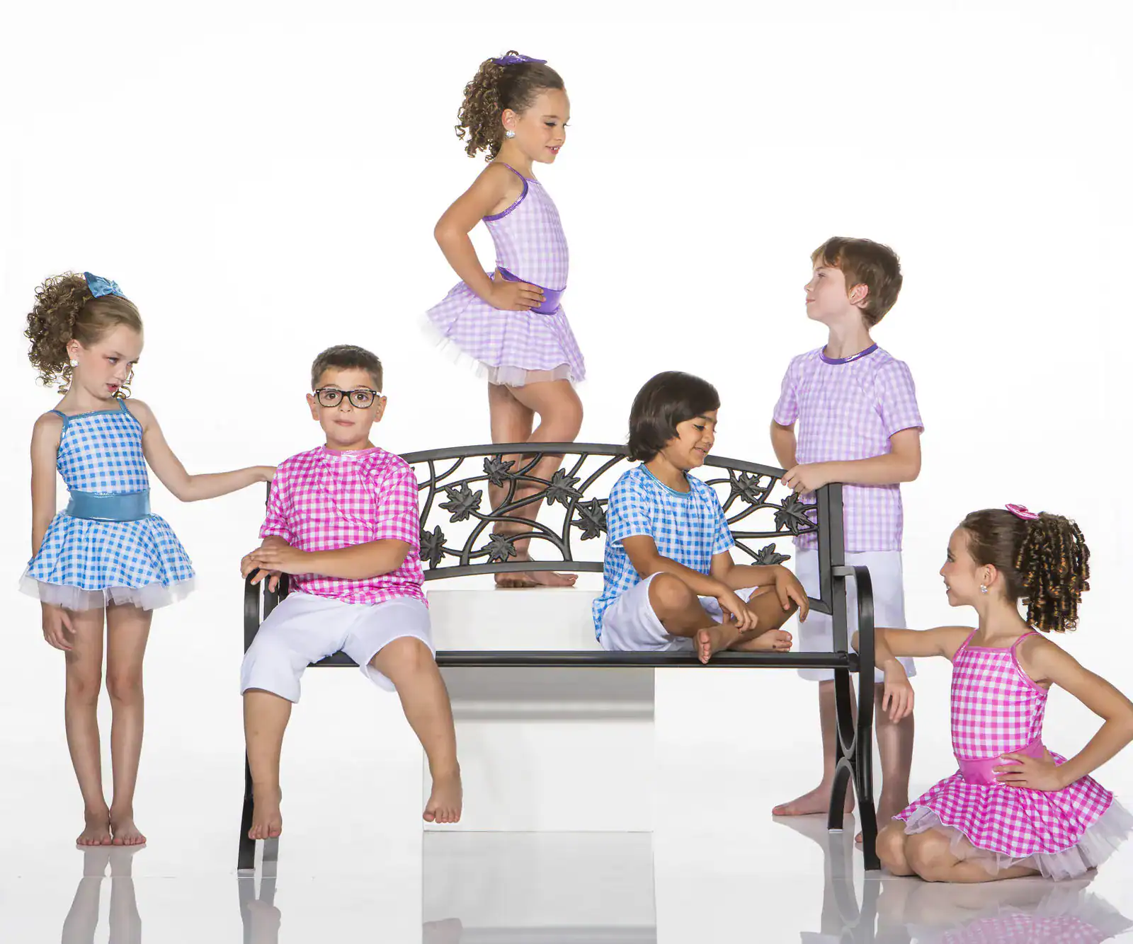 Six children in colorful gingham outfits pose around a bench.