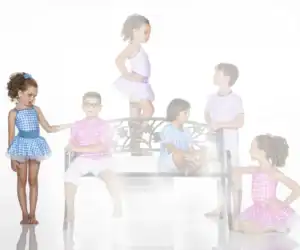 Children in colorful gingham outfits pose around a decorative bench.