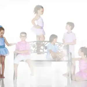 Children in colorful gingham outfits pose around a decorative bench.
