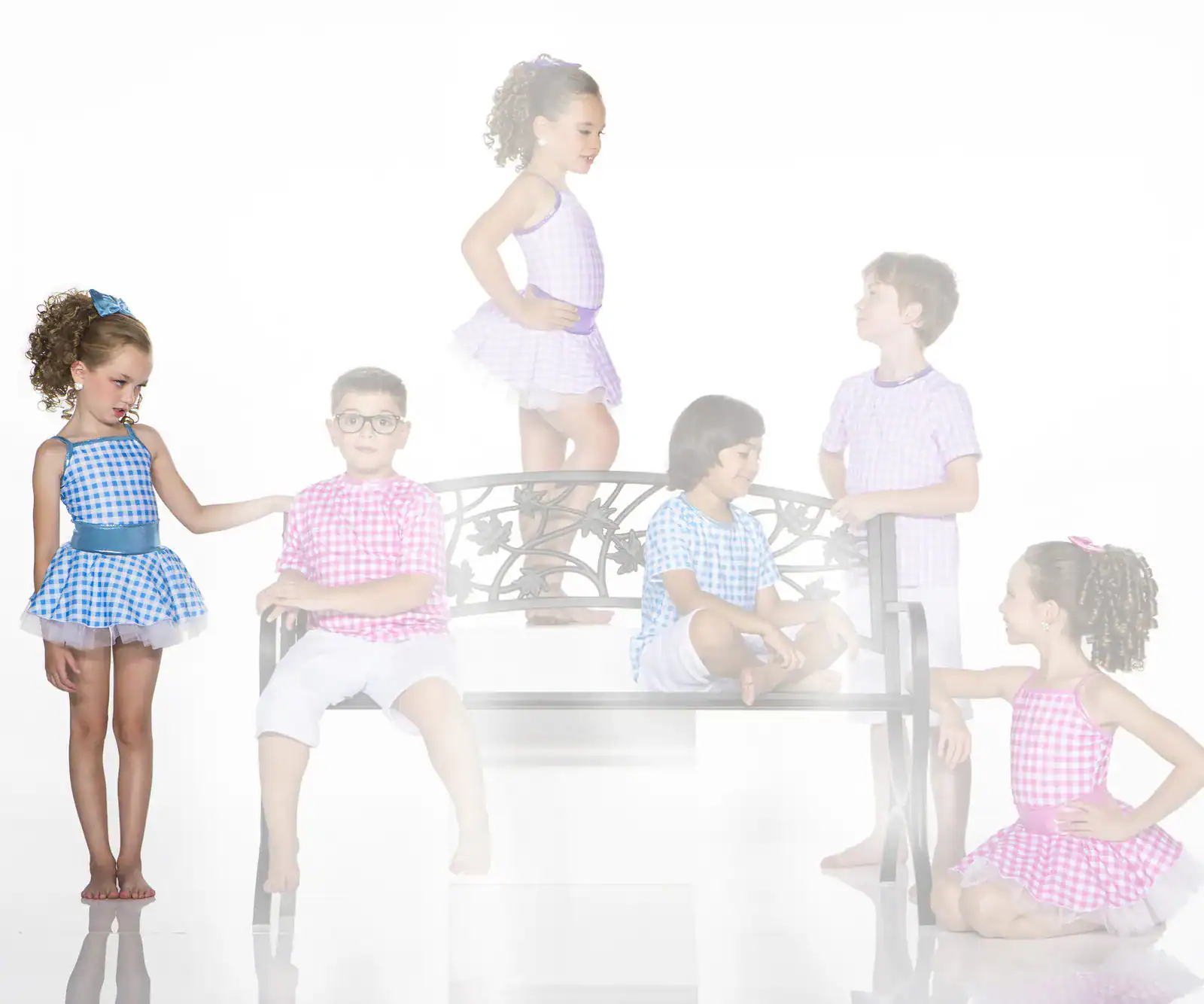 Children in colorful gingham outfits pose around a decorative bench.