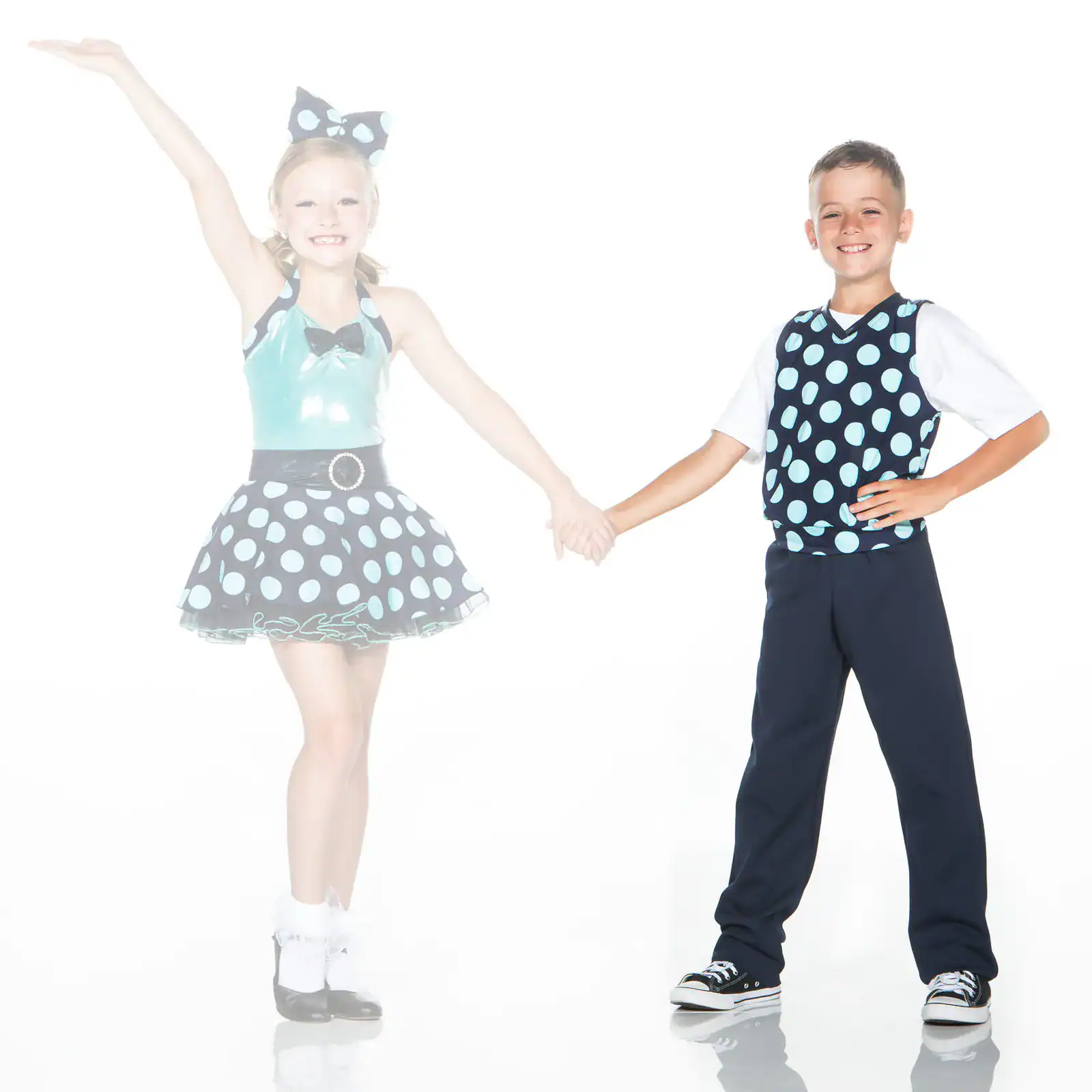 Two children holding hands in matching polka-dot dance costumes.