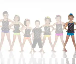Seven young dancers in colorful polka-dot costumes pose together.