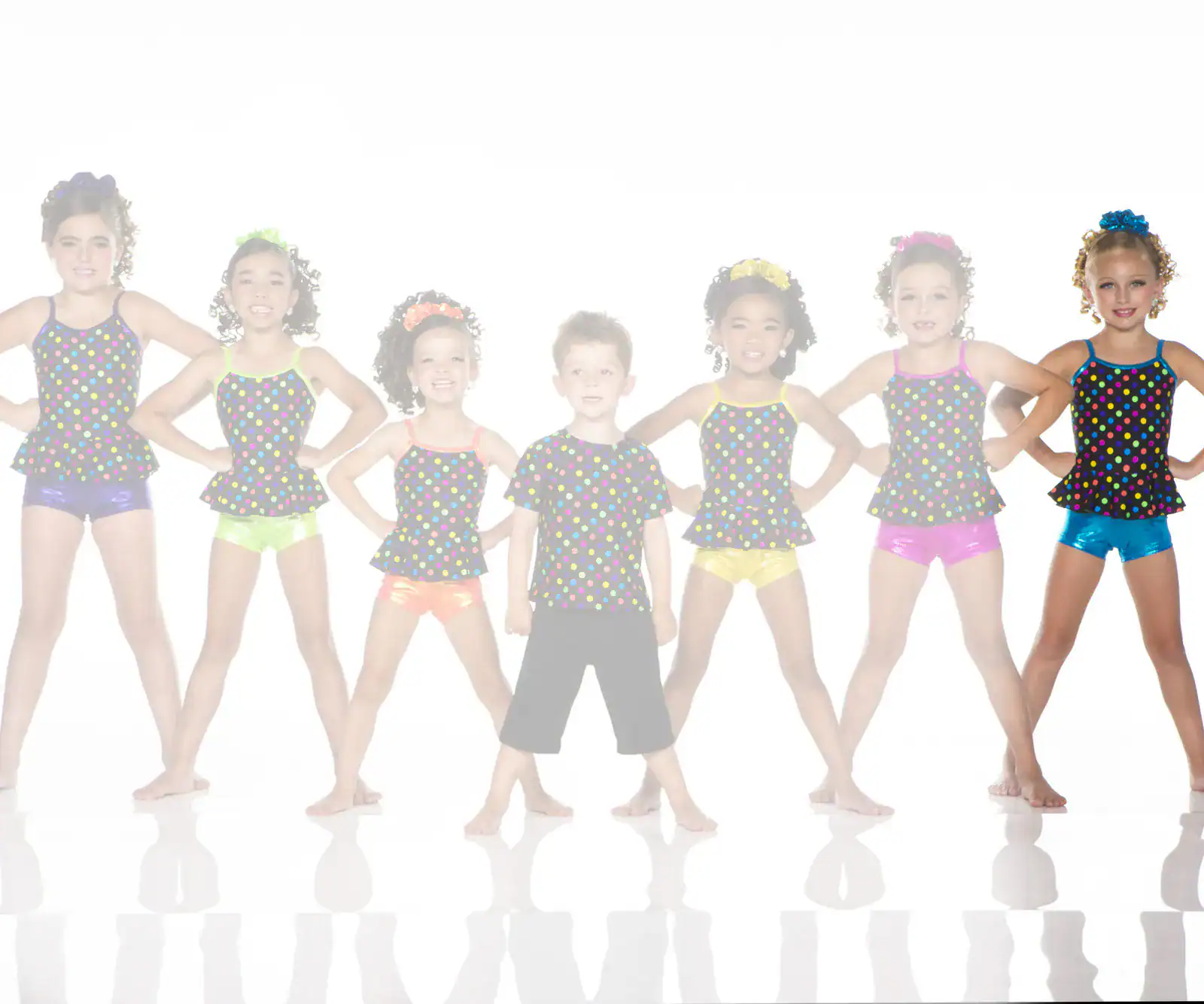 Seven young dancers in colorful polka-dot costumes pose together.