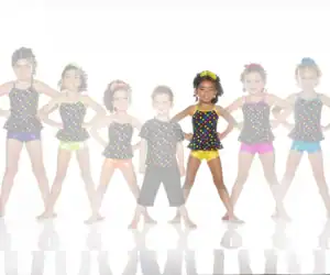 Seven children pose in colorful polka-dot dance outfits.
