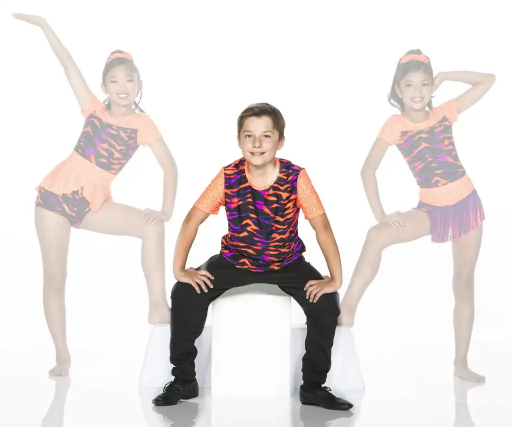 Boy seated between two young dancers in colorful costumes