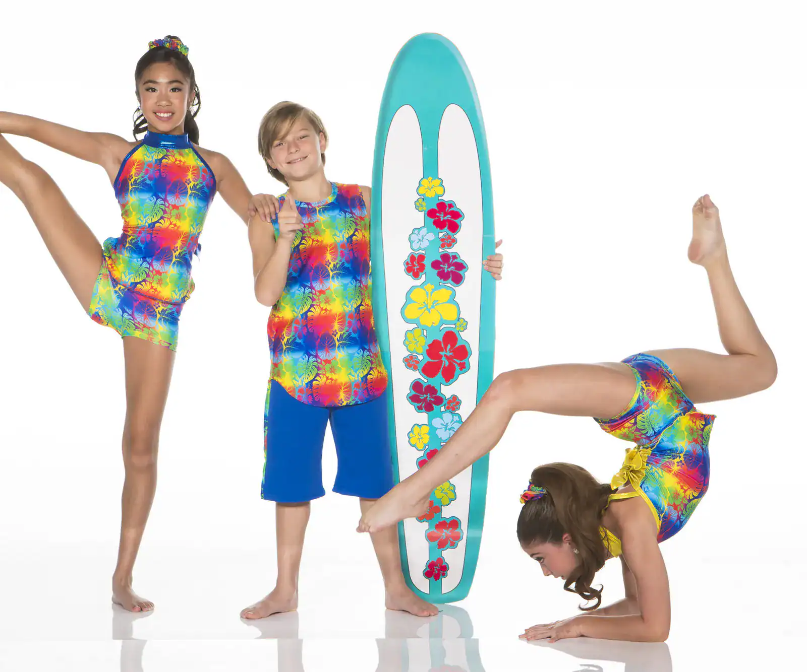 Three children in colorful outfits pose with floral surfboard.