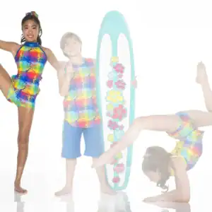 Children wearing colorful tropical outfits pose with surfboard