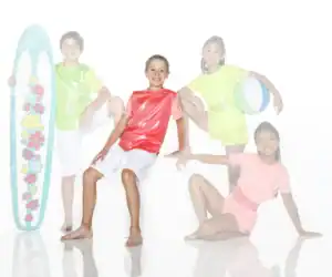 Four children in colorful beachwear pose with surfboard and ball.