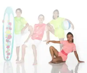 Children in colorful outfits pose with surfboard and beach ball