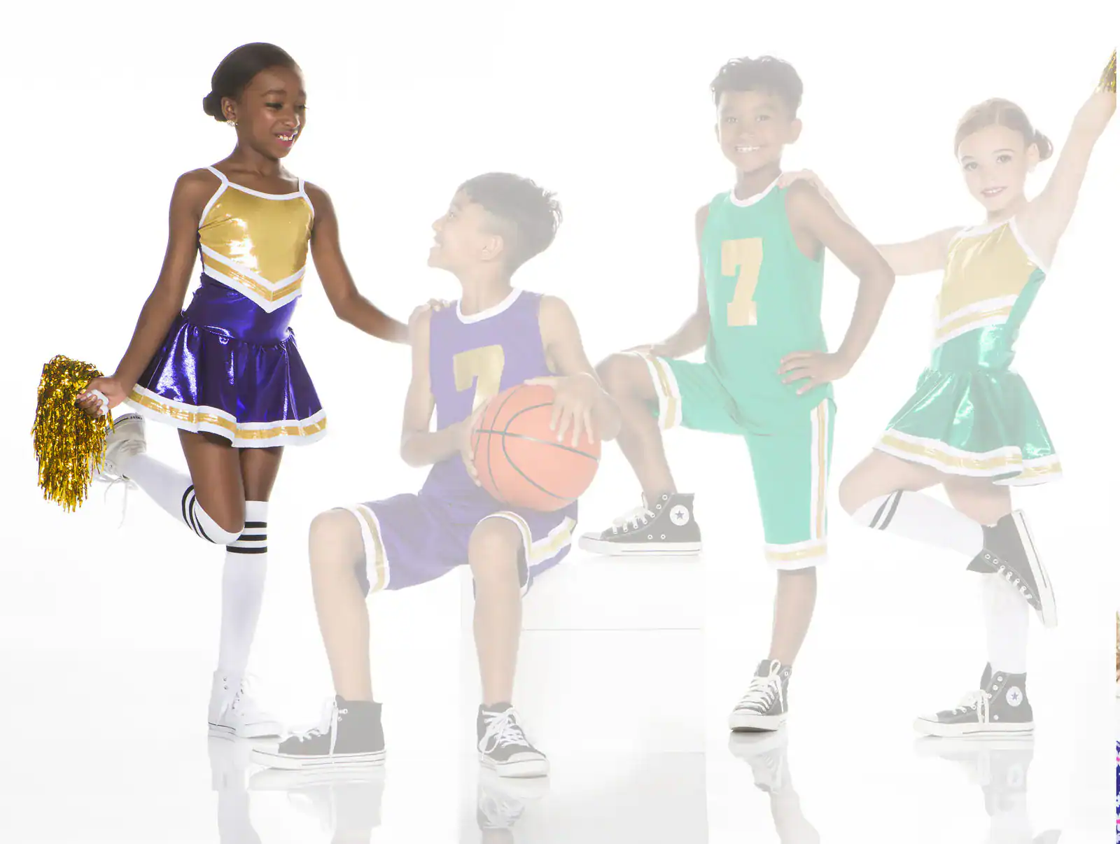 Four children in cheerleading and basketball uniforms posing together