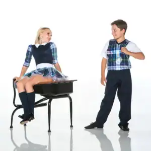 Two children wearing matching plaid school uniforms smile together.