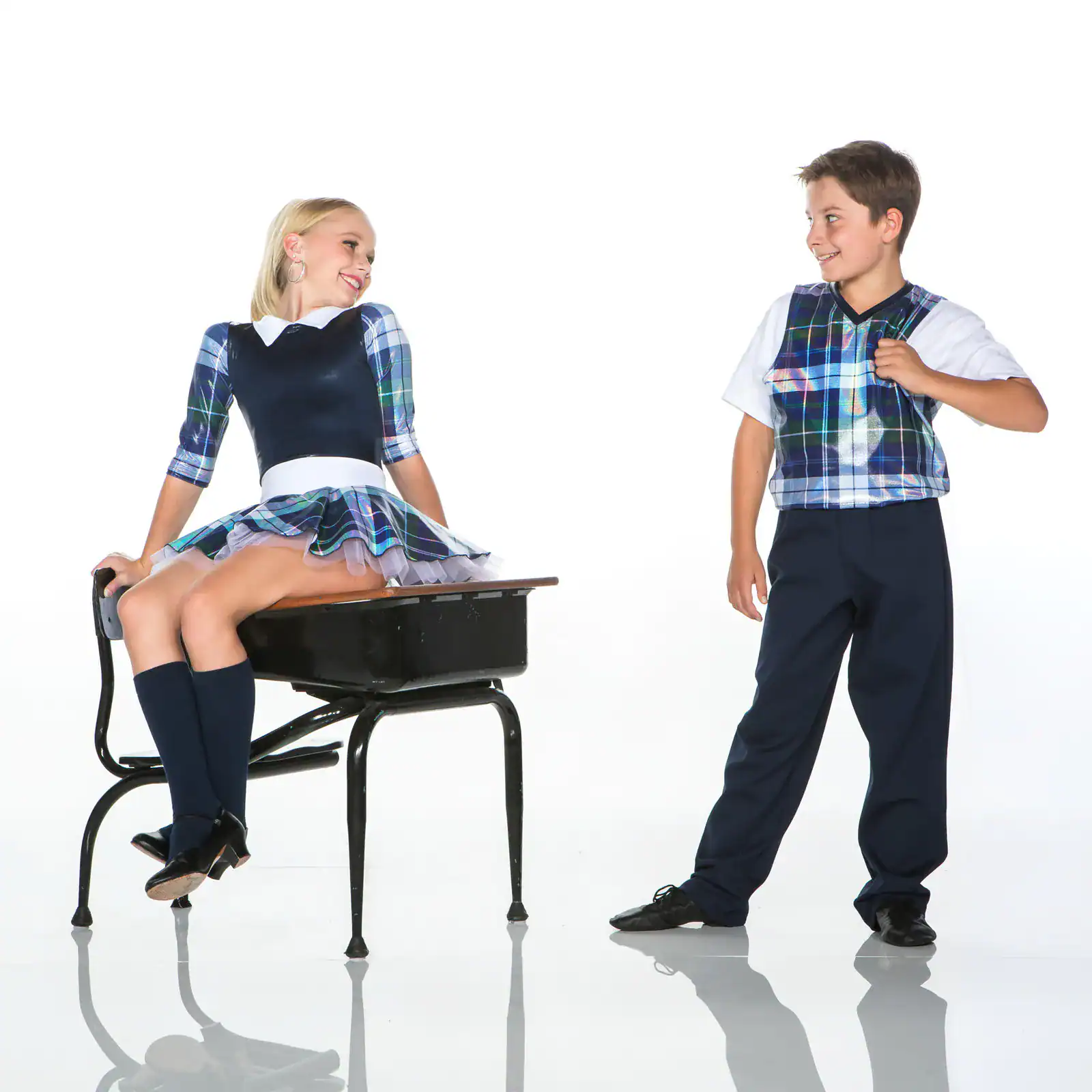 Two children wearing matching plaid school uniforms smile together.