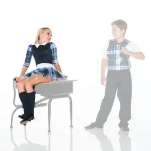 Students in plaid uniforms smiling beside a school desk