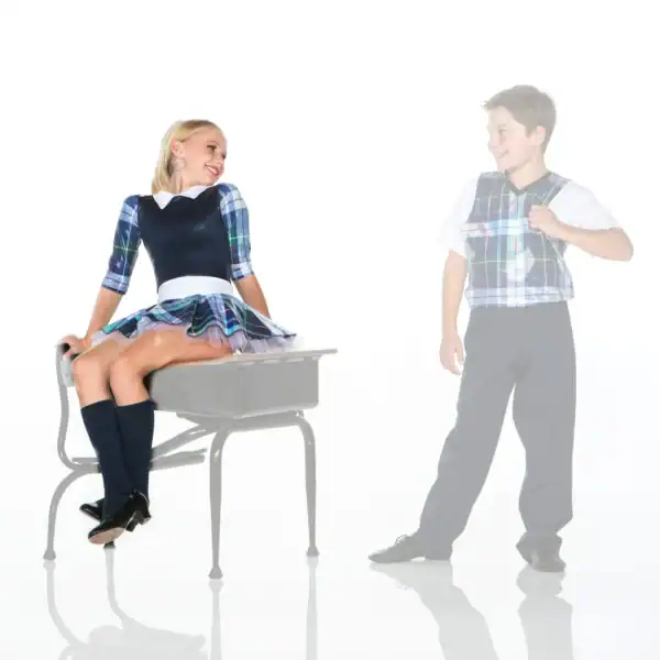 Students in plaid uniforms smiling beside a school desk