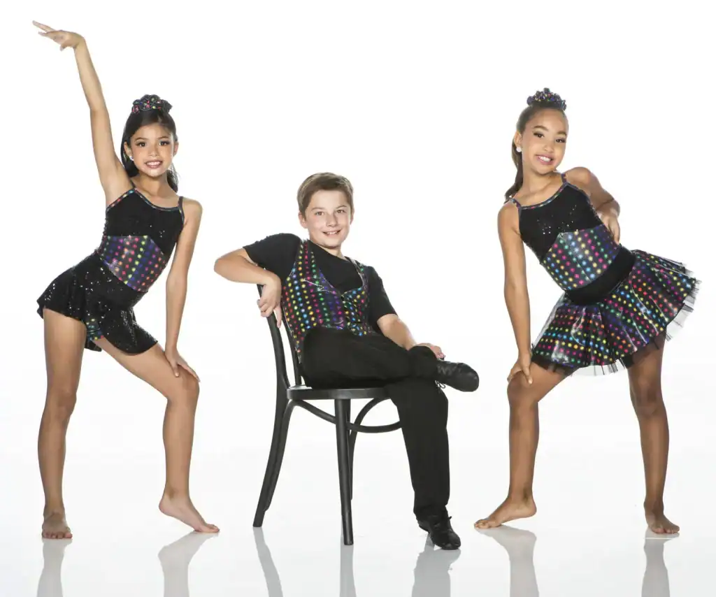 Three young dancers wearing colorful polka-dot costumes pose in studio.