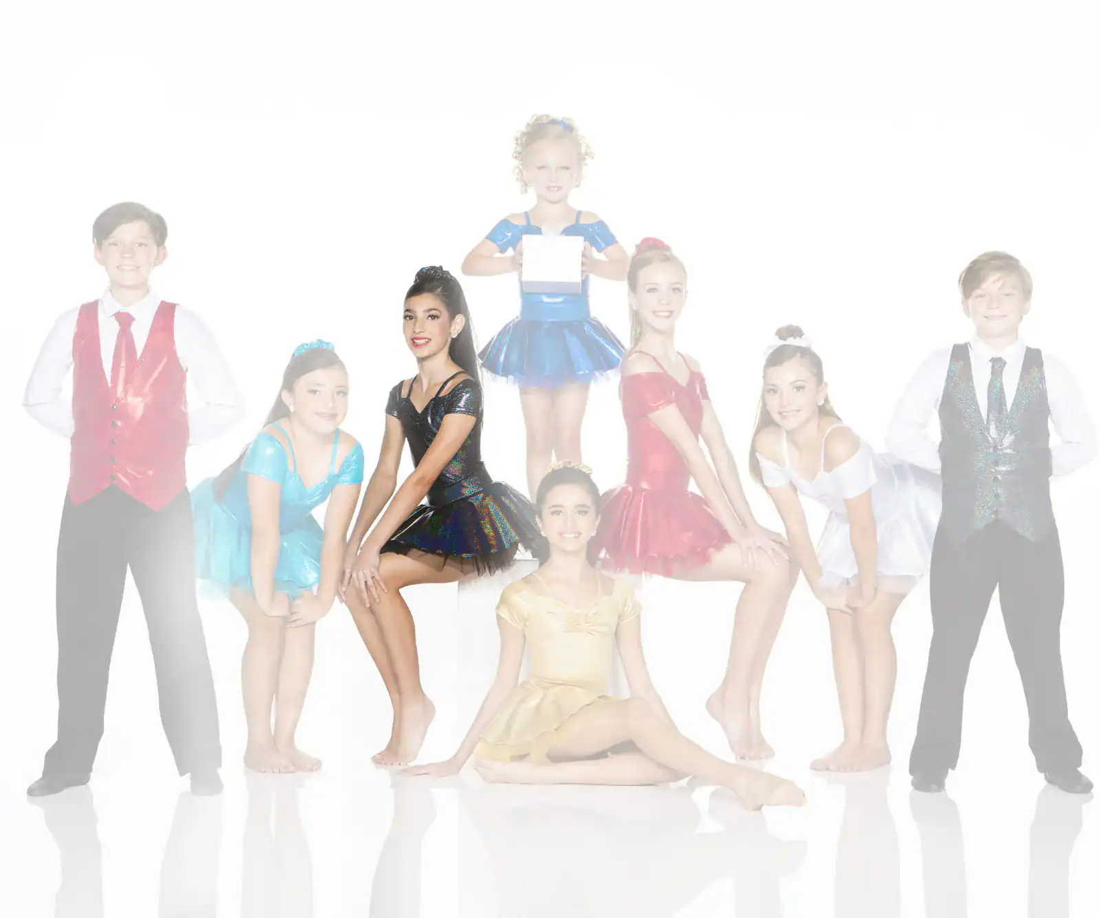 Eight young dancers pose in colorful costumes against white background.