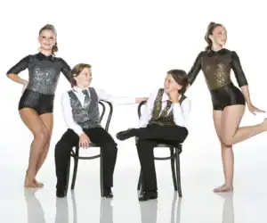 Four young dancers in sparkling costumes posing with chairs