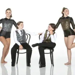 Four young dancers in sparkling costumes posing with chairs