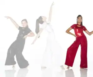 Three dancers pose in sparkling black, white, and red outfits.