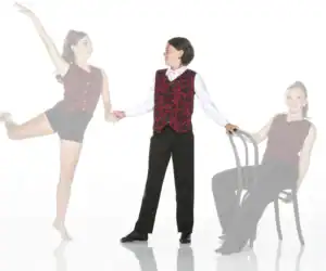 Dancers in matching red vests pose beside chair