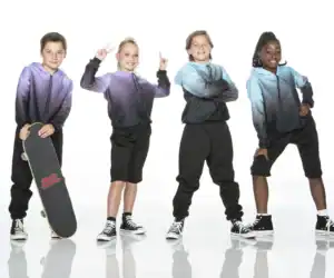 Four children in colorful hoodies pose with skateboard.