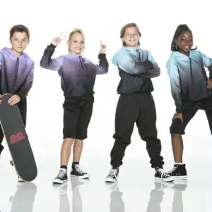 Four children in colorful hoodies pose with skateboard.