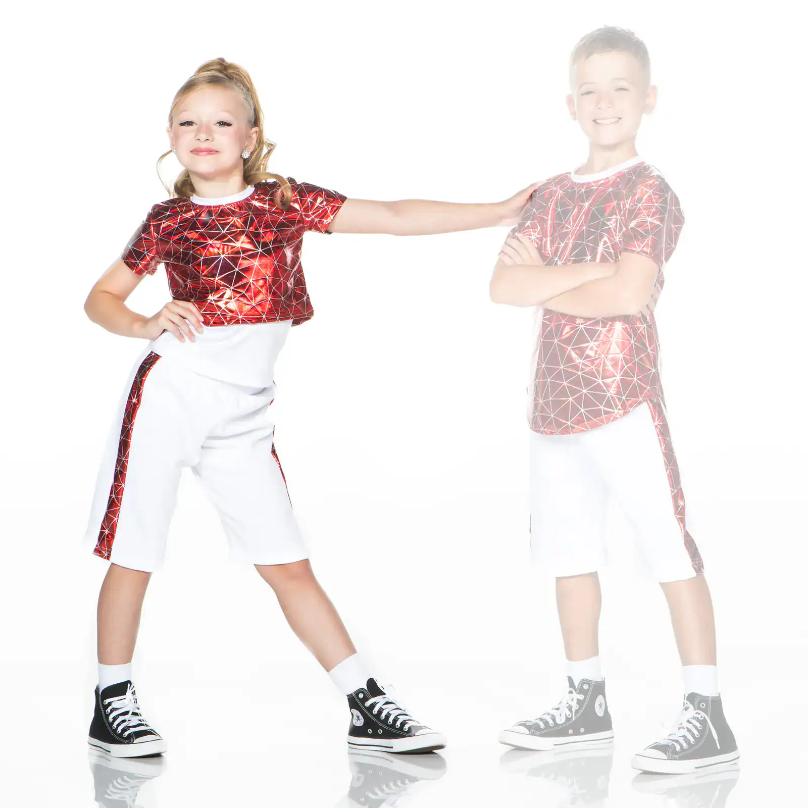 Two children wear matching red patterned shirts and white shorts.