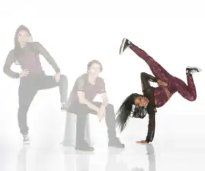 Three dancers pose in coordinated red and black outfits.