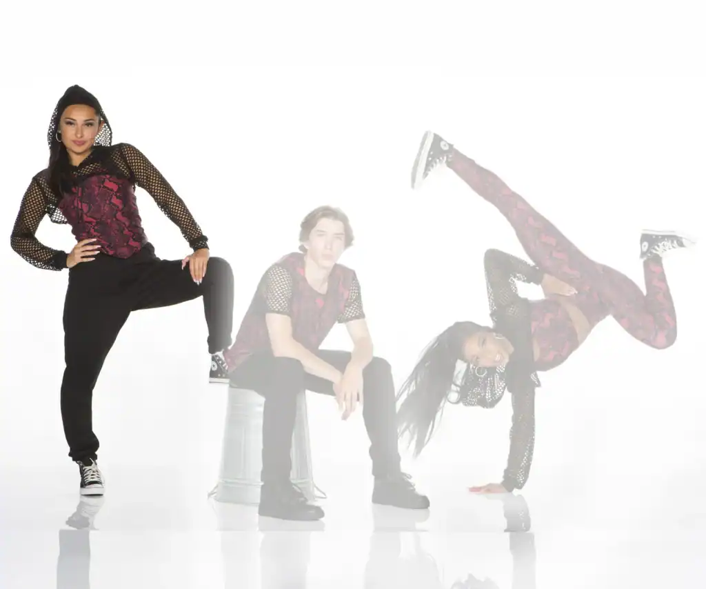 Three dancers pose in coordinated red and black outfits.