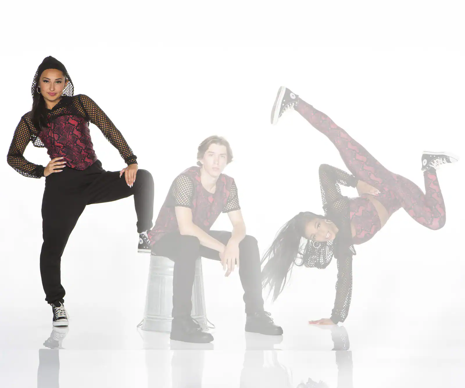 Three dancers pose in coordinated red and black outfits.