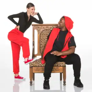 Two people in red and black outfits pose with ornate chair.