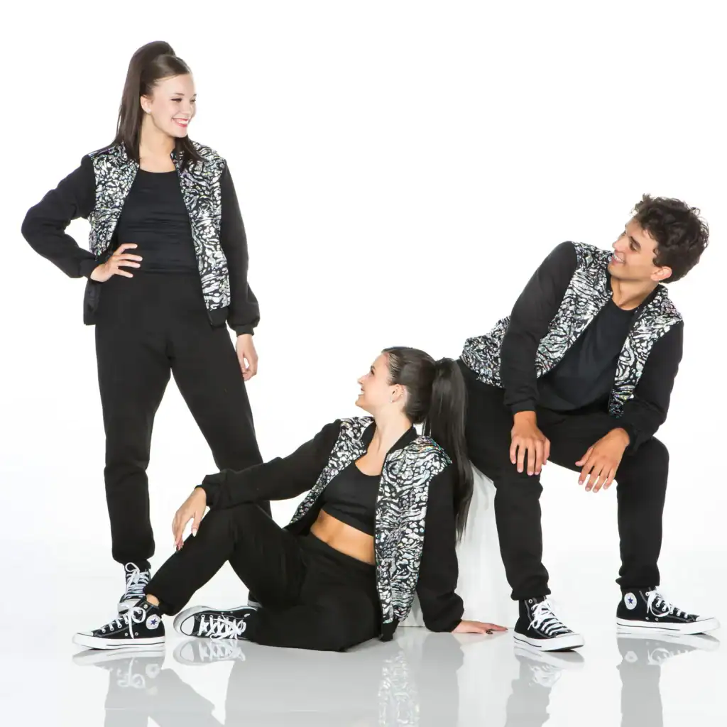 Three dancers in matching black reflective jackets pose together.