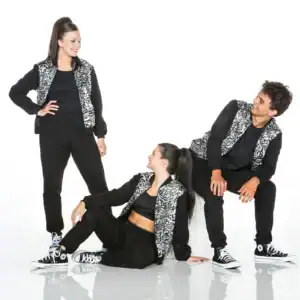 Three dancers in matching black reflective jackets pose together.