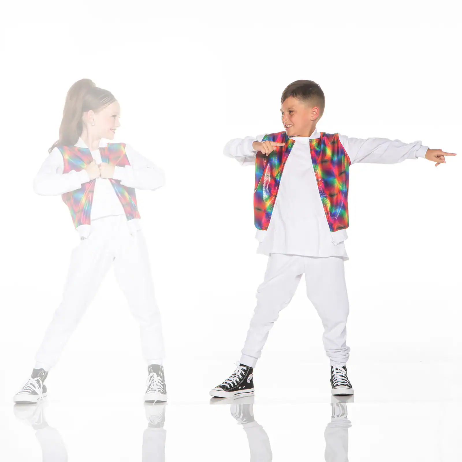 Two children wearing colorful vests and white outfits dance.