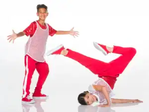 Two young dancers in red outfits pose on white background.